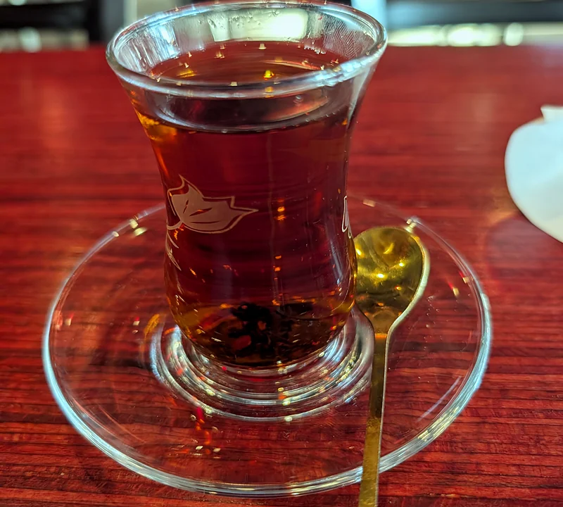 A glass of Persian tea on a glass saucer with a gold spoon