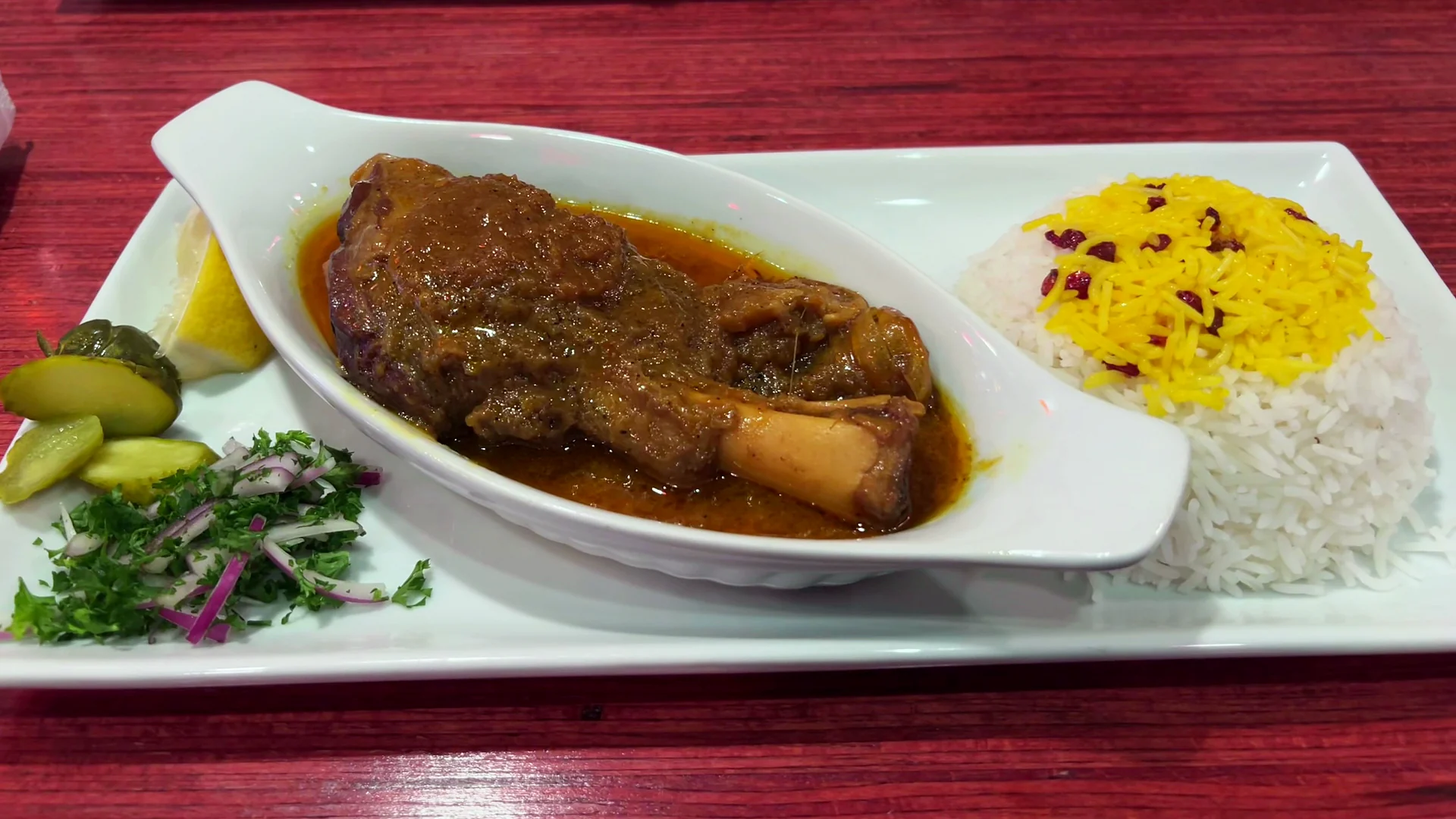 Plates of lamb shank with saffron rice on a red wood table