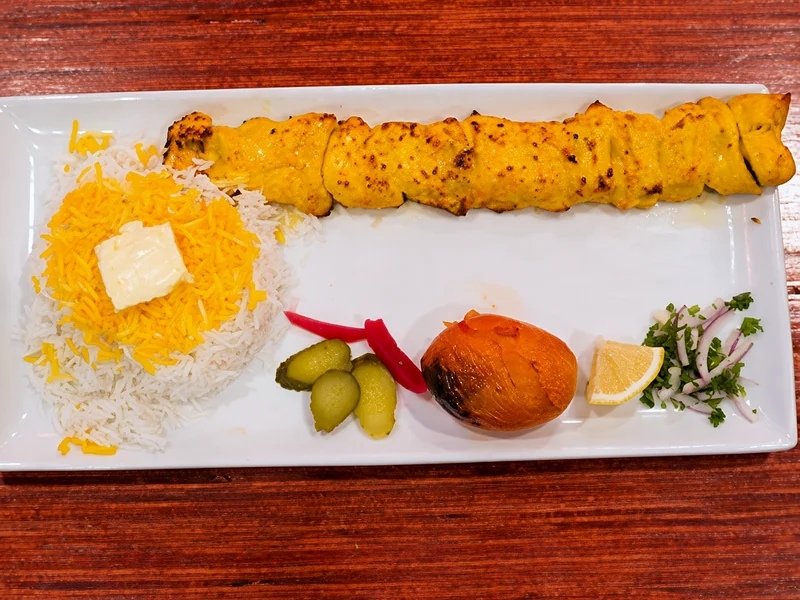 Joojeh kabab of saffron chicken breast with saffron rice and butter, grilled tomato, pickles and lemon