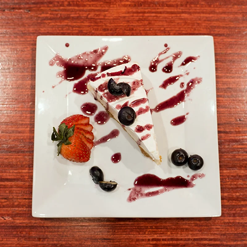 A slice of cheesecake with berry sauce, blueberries and a strawberry
