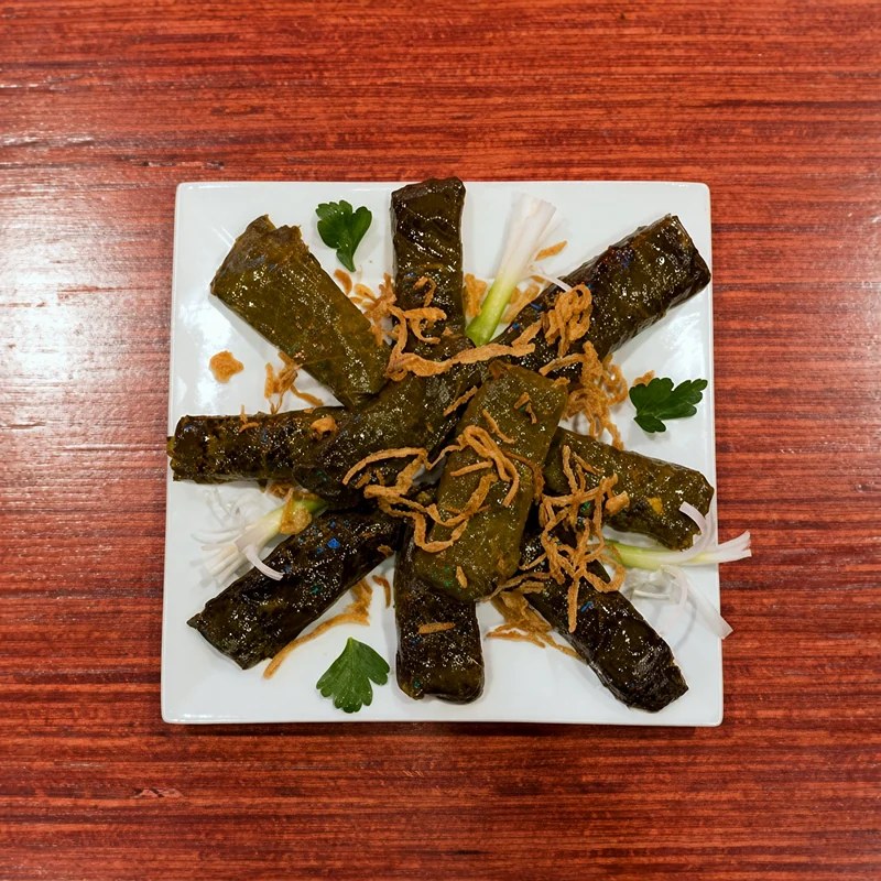 Dolmeh: stuffed vine leaves topped with fried onion on a square white plate