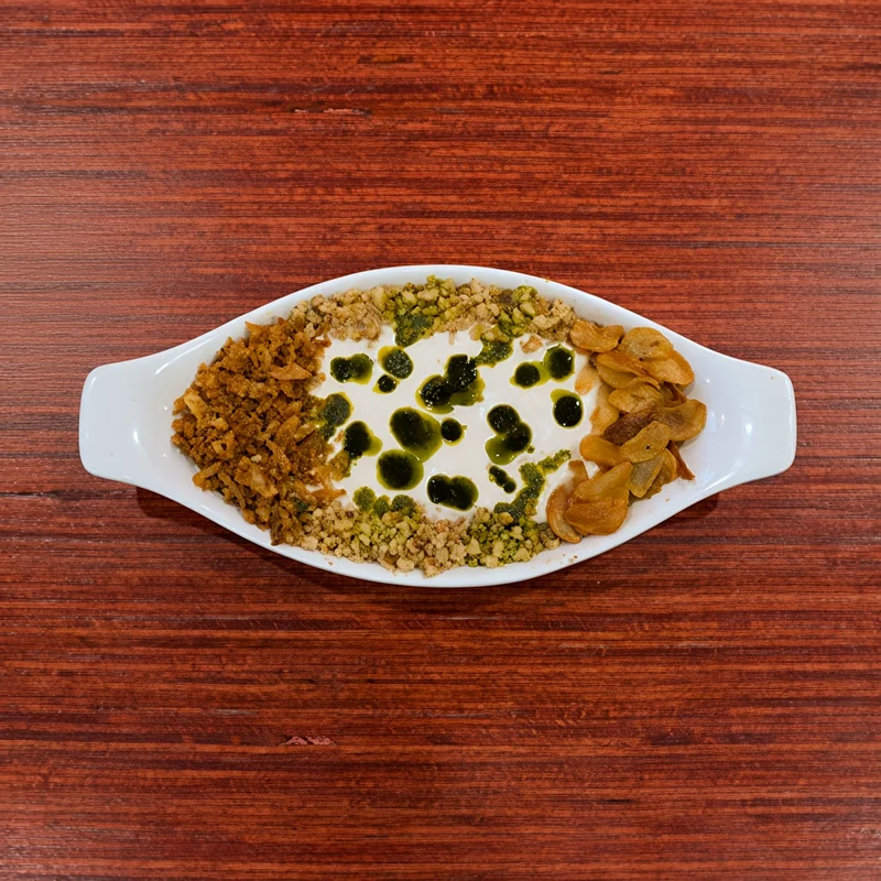 Kashk-e-bademjan eggplant dip topped with whey, fried onion, mint oil and walnuts in an oval dish