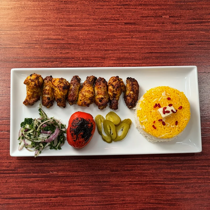 Grilled chicken wing kabab with saffron rice, a grilled tomato, pickles and onion salad