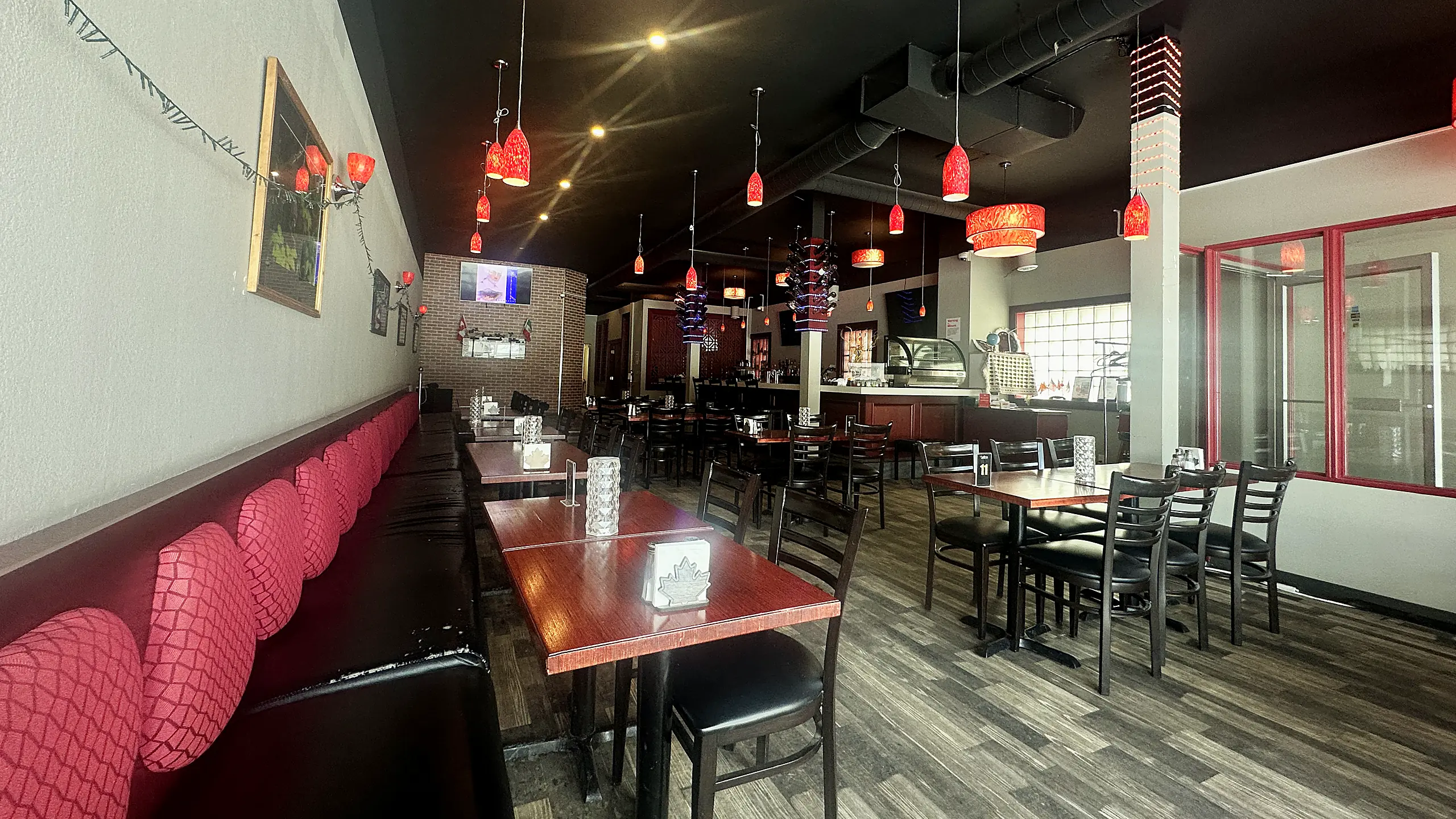 The dining room at Saffron, with red booth seating, wood tables and red glass pendant lights