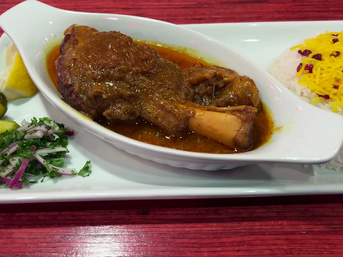 Chelo mahicheh: braised lamb shank in sauce in an oval dish, with saffron rice, pickles and herbs
