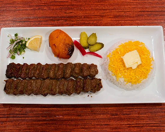 Two koobideh kababs with saffron rice and butter, a grilled tomato, pickles and onion
